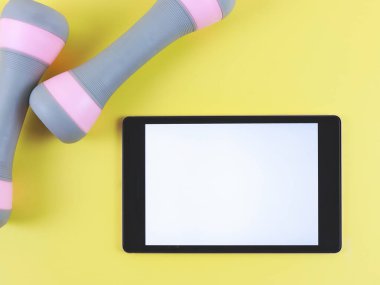 Beyaz ekran ve sarı arkaplanda izole edilmiş iki pembe gri dambıl ile dijital tabletin üst görünümü veya düz yatağı.