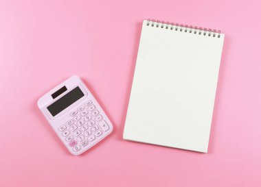 Pembe hesap makinesinin üst görünümü ya da düz yatay yatışı, boş sayfalı pembe arkaplan üzerine açık bir defter. işletme ve eğitim kavramı.