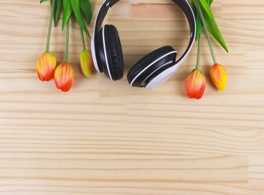 Beyaz kulaklıkların üst görüntüsü ve kırmızı sarı lale çiçekleri ahşap masa zemininde fotokopi alanı ile. Aşk şarkısı, bahar müziği, podcast ve sesli kitap.