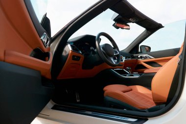 Açık sürücü kapısından görülebildiği üzere, üstü açık beyaz bir arabanın içinde kahverengi bir iç mekan.