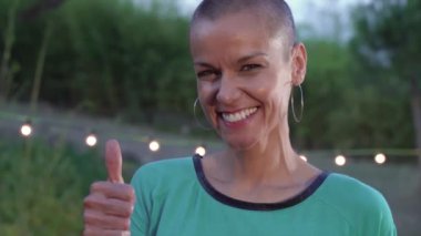 Kafası tıraşlı bir kadının portresi başparmağını kaldırıyor ve kameraya ağır çekimde güçlü jestler yapıyor. Yüksek kalite 4k görüntü