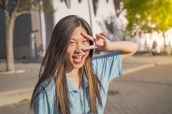 迷人的亚洲女孩在校园里微笑着看着相机的胜利手指 高质量的照片 — 图库照片
