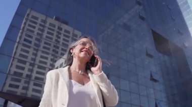 Modern bir binanın önünde akıllı telefonuyla konuşan mutlu çekici bir iş kadını. Yüksek kalite fotoğraf