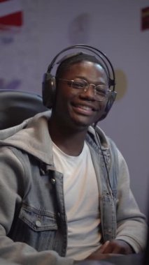 Genç siyahi adamın gülümseyen ve gülen videosunun dikey bir portresi. Kendi ses stüdyosundaki Z Nesli etkilenen blogunda kameraya bakıyor. Sesli kitap kaydı. Yüksek kaliteli görüntüler