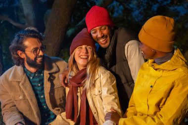 Kafkasyalı ve siyah çiftlerin olduğu gece şenlik ateşinin yanında gülerek mutlu arkadaşlar edinin. Kamp, müzik, doğa ve arkadaşlık kavramı. Yüksek kalite fotoğraf