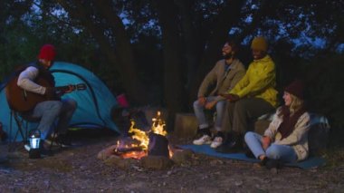 Mutlu çoklu etnik arkadaşlar müzik çalarak ve gece kamp kurarak eğleniyorlar. Bir grup insan gece ormanda takılıyor. RED kamerada yüksek kaliteli video görüntüsü