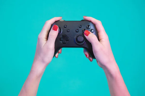POV of female hands gaming with video game controller gamepad isolated on a blue background studio. Red nails black button joystick. High quality photo