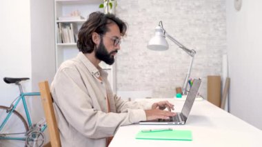 Evdeki uzaktan kumandalı bilgisayarı kullanan bir adam. Araştırmayla ilgili yaratıcı bir projede çalışan yakışıklı, gülümseyen serbest girişimci erkek. Yüksek kalite 4k görüntü