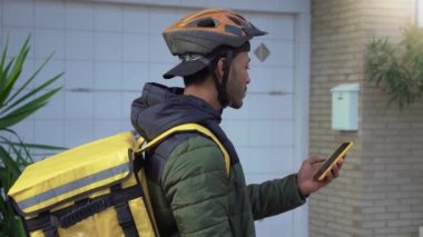 Yemek teslimatı konsepti. Sırt çantalı genç bir Afro-Amerikan şoför akıllı bir telefonla online alışveriş sipariş eden müşterilere ürünler getiriyor. Siyahi erkek işinden memnun..