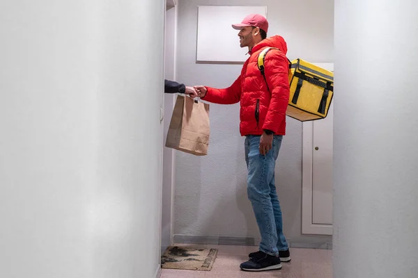 Food delivery concept. Young smiling African American driver with backpack delivering products at door for customers who order online purchases. Black male happy with his job.