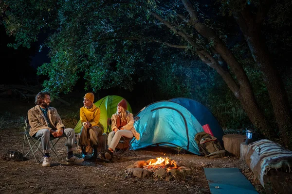 Multiethnic friends sitting around camp fire in the woods. Enjoying nature having fun together camping. Travel and nomad adventure concept. High quality photo