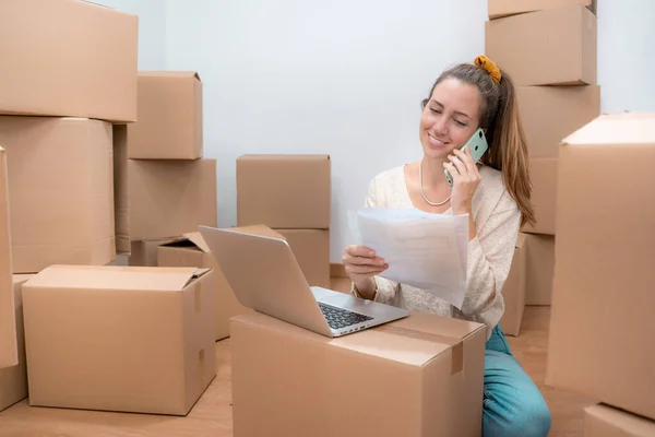 Beautiful girl with cardboard boxes unpacking in new home - Working with laptop . High quality photo