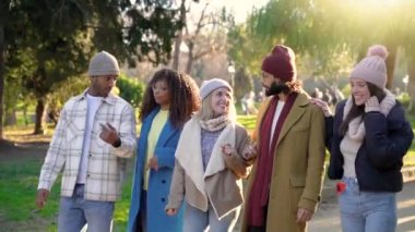 Cheerful group of friends walking outdoors in the park having fun together. Happy people talking with positive expression. Concept of community, youth lifestyle and friendship. High quality photo