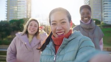 Three girls taking a selfie portrait looking at camera. An Asian Chinese woman, a black African and a Caucasian lady together and embracing. Friendship multi-ethnic group of people.