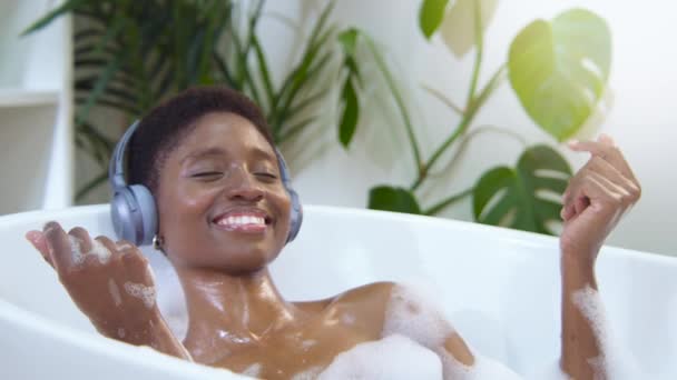 Smiling African Attractive Woman Wearing Headphones Relaxing Dancing Foam Bath — Vídeo de Stock