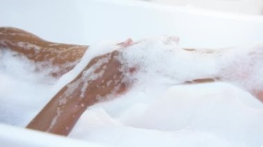 Closeup of a black womans arm caressing herself in a white foam bathtub in slow motion. Morning routine. Clean skin care concept. 4K footage shot on RED camera.