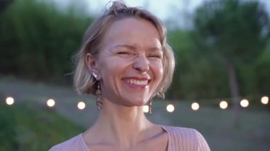 Portrait of attractive blonde woman smiling and laughing looking at camera outdoors in slow motion. Real people. High quality 4k footage