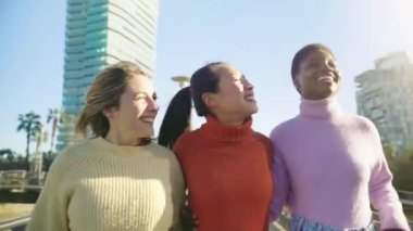 Three female friends walking arm in arm outdoors in the city during a sunny day. Leisure and freedom concept. High quality 4k footage
