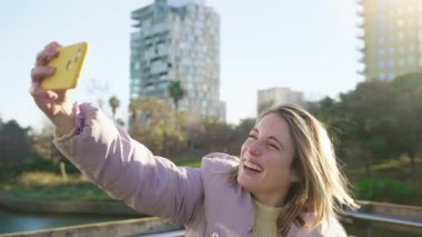 Woman taking selfie for a video call or blog with smartphone outdoors in the city. Happy influencer girl smiling, kissing and saying hello to the viewers. High quality 4k footage