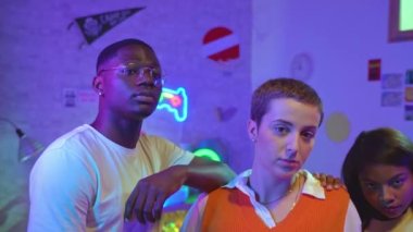 Portrait of three attractive young friends posing looking et camera in a gaming room with neon lights. Professional video games team.