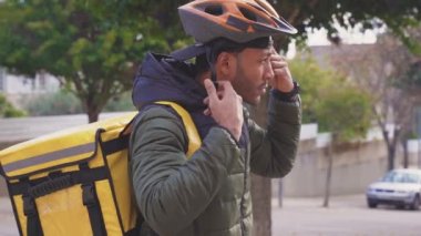 Food delivery concept. Young black man driver with backpack putting helmet on in the city to deliver products for customers who order online purchases. Black male happy with his job.
