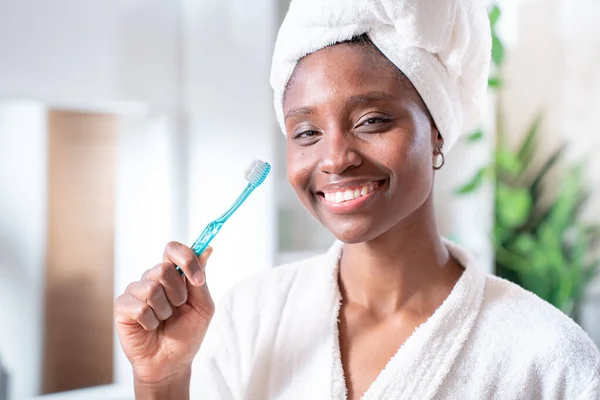 Teeth care and oral hygiene concept. Positive young Afro American woman holds toothbrush, beautiful smile, cleans teeth, has dark skin, being in high spirit. Healthcare and dentistry. High quality