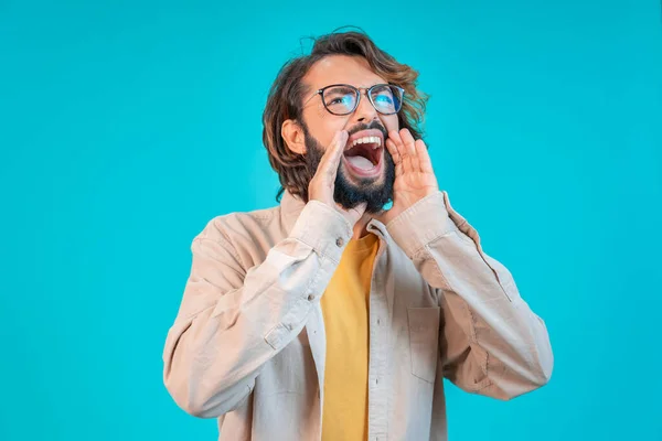 Man shouting loud calling attention with hands in the shape of a megaphone isolated on blue studio background with copy space for text. High quality photo