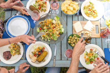 Ahşap masada oturan arkadaşların en iyi görüntüsü. Arkadaşlar yemek yiyor. Yiyecek dolu tabakları ve içeceklerle dolu bardakları var. Yüksek kalite fotoğraf