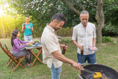 Barbeküyle yemek pişiren arkadaşlar mutlu mesut gülüyorlar ve açık havada verandada birlikte gülüyorlar. Yüksek kalite fotoğraf