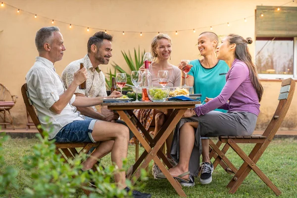 Friends eating and drinking happy smiling and laughing in the patio. Mature cheerful people around the table. High quality photo