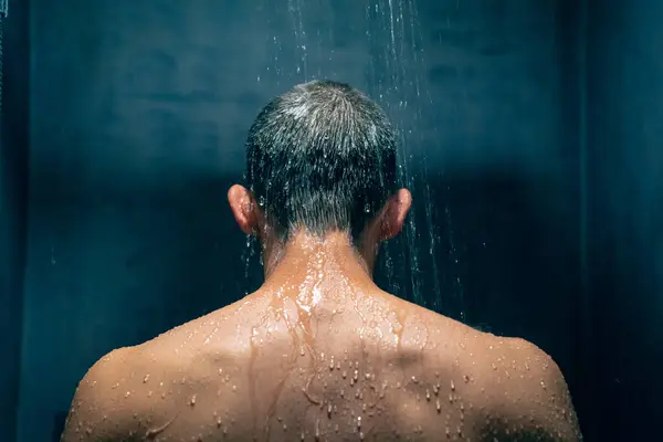 Man taking a shower relaxing under water falling from rain shower head. Guy showering body care hygiene concept.