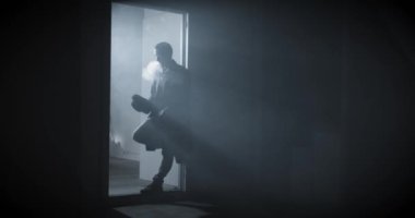 Kara film dedektifi karanlıkta dikilip sigara içiyor. Yağmurluk giyiyor. Yüksek kalite 4k görüntü