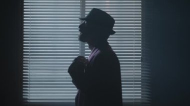 Kara casus film karakteri, pencere arkasının yanındaki karanlık bir odada şapka takıyor. Yüksek kalite 4k görüntü