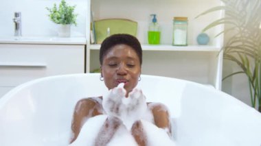 Siyah kadın köpükle dolu bir küvette mutlu bir banyo yapıyor. Yüksek kalite 4k görüntü
