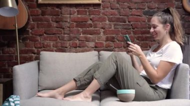 Evde akıllı telefon cihazıyla cep telefonu tutan mutlu İspanyol genç kız. Gülümseyen genç bir kadın yeni sosyal medya aboneliği, internetten satın alma, internetten ürün sipariş etme. Yüksek kalite 4k görüntü