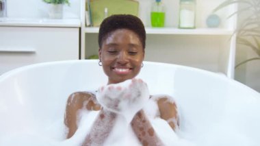 Siyah kadın küvette banyo yaparken köpükle eğleniyor. Yüksek kalite 4k görüntü