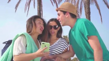 Modayı takip eden genç arkadaşlar yazın plajda akıllı telefonlar ve sosyal medya oynayarak eğleniyorlar. Yüksek kaliteli FullHD görüntüler