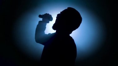 Yetenekli müzisyen, mikrofonla tutkuyla şarkı söyleyerek çarpıcı bir siluet yaratıyor. Yüksek kalite 4k görüntü