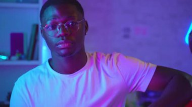 Portrait of three attractive young friends posing looking et camera in a gaming room with neon lights. Professional video games team.