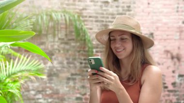Gülümseyen Kadın, Çevresi yemyeşil bir ayar ile çevriliyken mutlu bir şekilde akıllı telefonunun tadını çıkarıyor. Yüksek kalite 4k görüntü