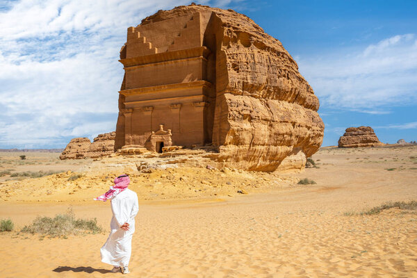 Arab man in front of Tomb of Lihyan, son of Kuza carved in rock in the desert,  Mada'in Salih, Hegra, Saudi Arabia