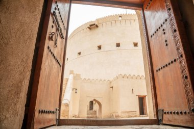Süslü ahşap kapıların arasından Arap kalesinin iç bahçe kulelerine ve duvarlarına bak. Crenellasyonlu, Nizwa, Sultan Umman.