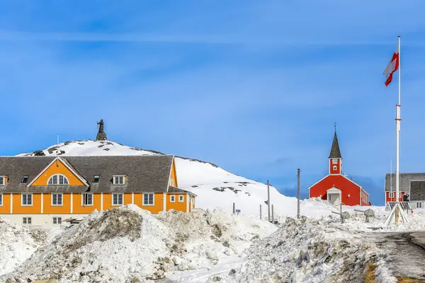 Kar arasında yeşil bayraklı kırmızı ve sarı binalar, Annaassisitta Oqaluffia, Kurtarıcımız Nuuk, Grönland Tarihi Merkezi Kilisesi