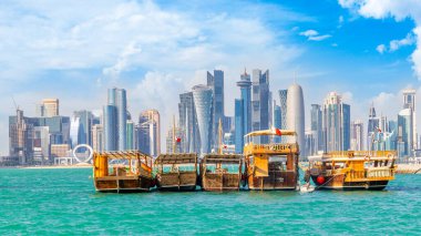 Geleneksel Arap dhow balıkçı tekneleri Katar şehir merkezindeki Doha fütüristik iş merkezi silueti ile deniz koyunda Katar bayrağı taşıyor.
