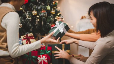 Bir grup mutlu Asyalı arkadaş Noel 'i kutluyor ve Noel ağacını içeride süslüyor. Noel hediyeli güzel kadın. Yeni yıl partisi. Kadın elleri Noel ağacını süslüyor Kırmızı top, takı gibi.