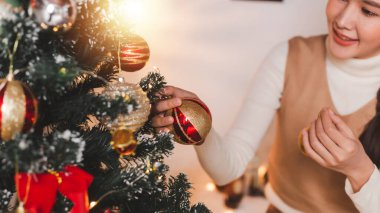 Bir grup mutlu Asyalı arkadaş Noel 'i kutluyor ve Noel ağacını içeride süslüyor. Noel hediyeli güzel kadın. Yeni yıl partisi. Kadın elleri Noel ağacını süslüyor Kırmızı top, takı gibi.