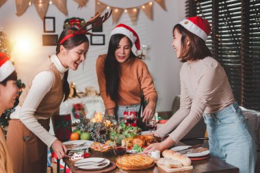 Yetişkin bir grup Asyalı genç arkadaş evde, masanın etrafında tatil yemeği yiyorlar. Noel 'i kutlayalım. İnsanlar Noel arifesinde yemek hazırlıyor konuşuyorlar ve neşeyle gülüyorlar..