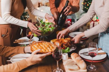 Yetişkin bir grup Asyalı genç arkadaş evde, masanın etrafında tatil yemeği yiyorlar. Noel 'i kutlayalım. İnsanlar Noel arifesinde yemek hazırlıyor konuşuyorlar ve neşeyle gülüyorlar..