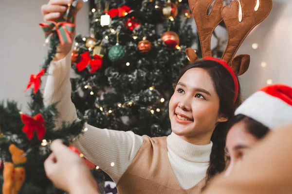 Bir grup mutlu Asyalı arkadaş Noel 'i kutluyor ve Noel ağacını içeride süslüyor. Noel hediyeli güzel kadın. Yeni yıl partisi. Kadın elleri Noel ağacını süslüyor Kırmızı top, takı gibi.