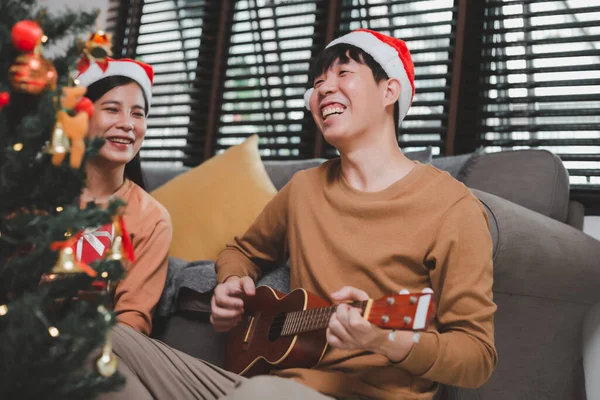 아시아 청년들이 크리스마스 이브를 축하하는 거실에서 우쿨렐레를 연주하며 즐거운 시간을 — 스톡 사진